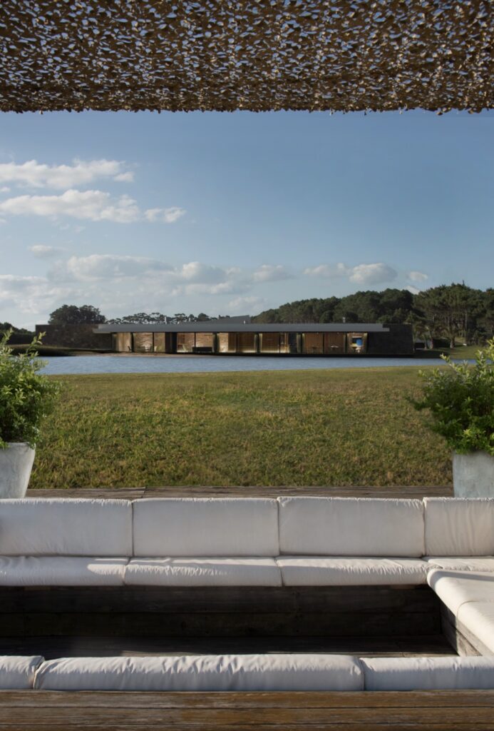 Vista del Beach House de Las Cárcavas, donde se encuentra el restaurante y el espacio para eventos, con la laguna en un día soleado, fotografiada desde la pérgola en la playa.